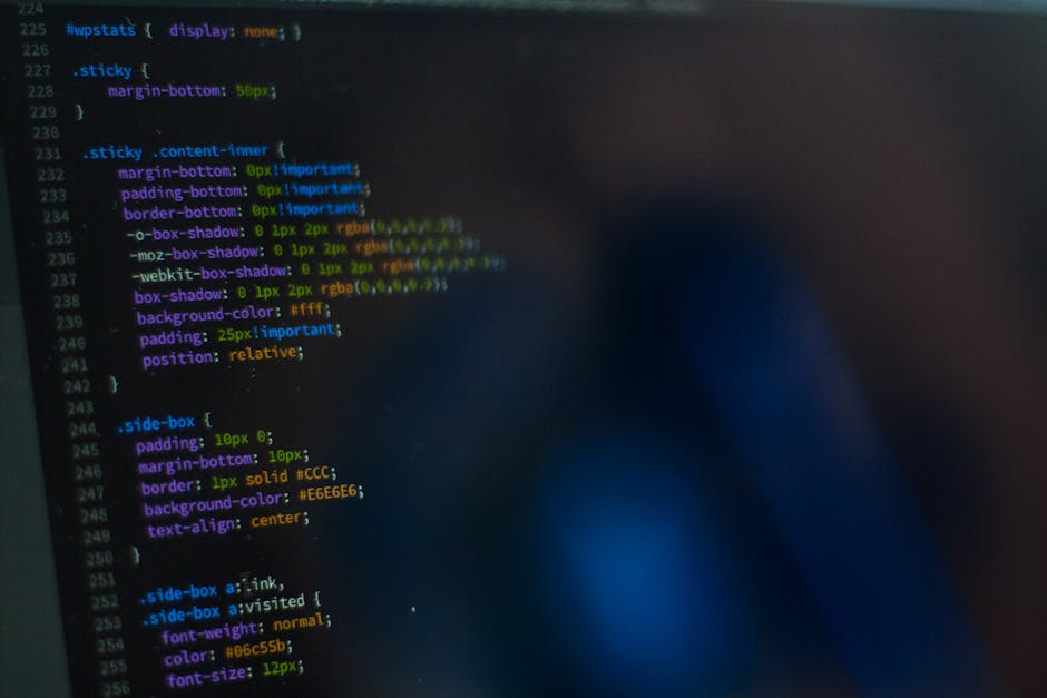 A close-up photograph of a computer screen displaying lines of colorful code in a text editor, with syntax highlighting in shades of blue, green, yellow, purple, and orange. The code appears to be rel